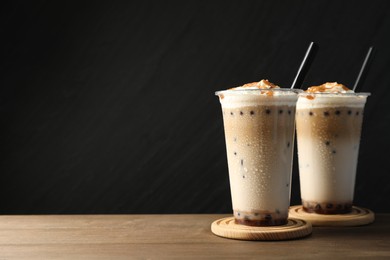 Photo of Tasty milk bubble tea in plastic cups on wooden table. Space for text