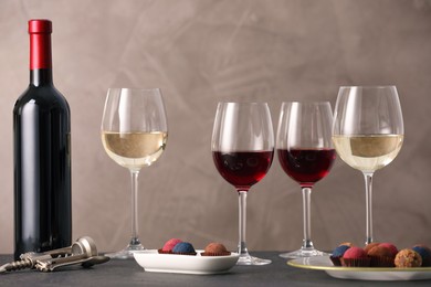 Photo of Delicious truffle bonbons and wine on black table against grey background