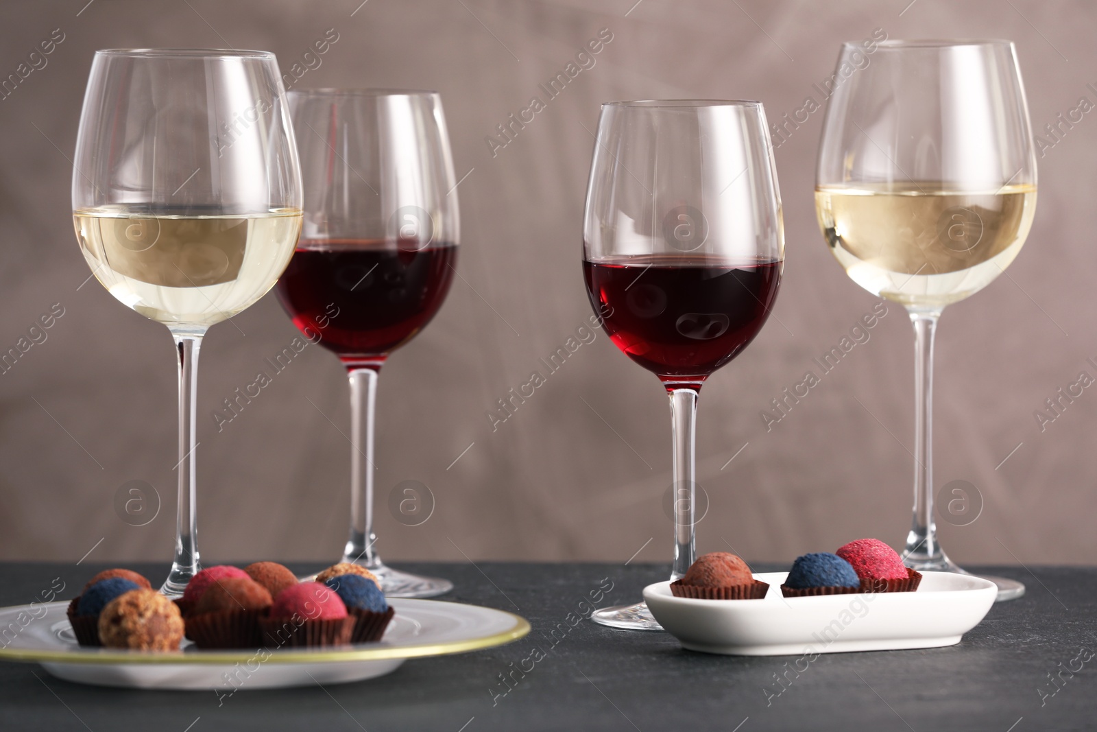 Delicious truffle bonbons and wine on black table against grey background Photo of Delicious truffle bonbons and wine on black table against grey background