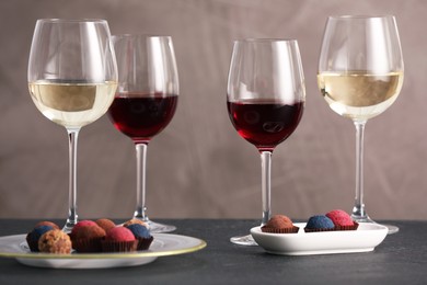 Photo of Delicious truffle bonbons and wine on black table against grey background