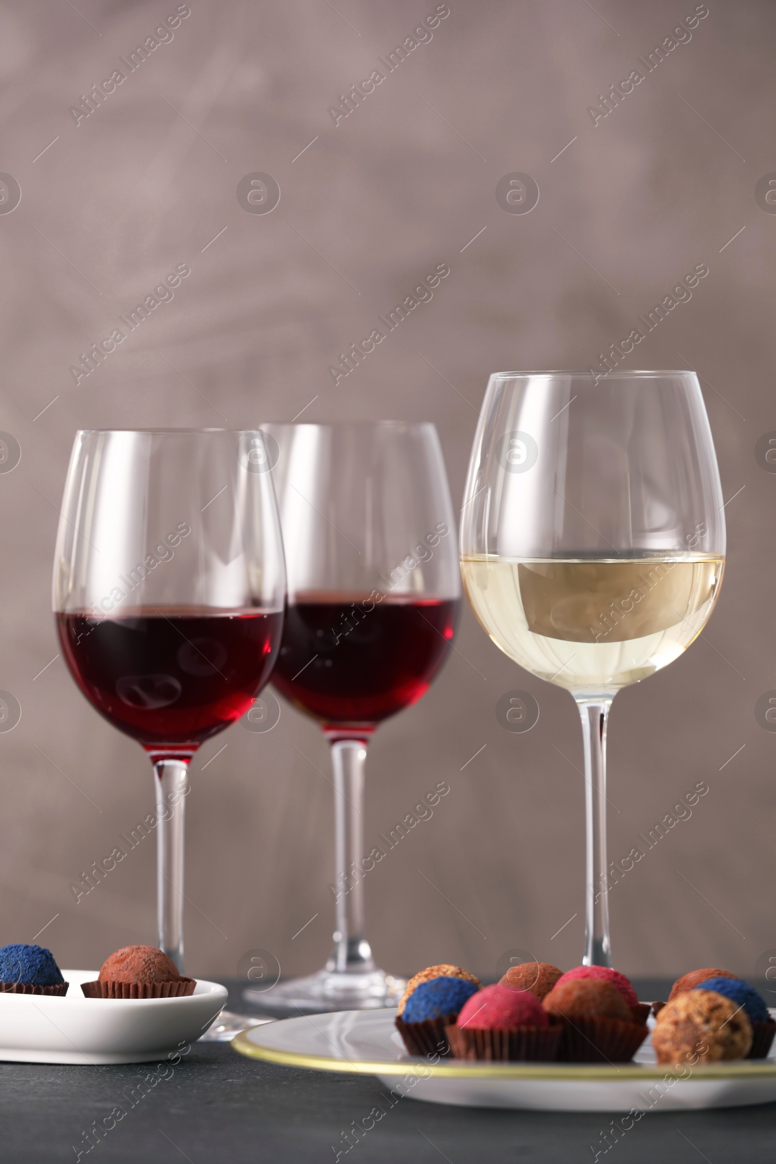 Photo of Delicious truffle bonbons and wine on black table against grey background