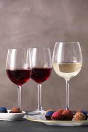 Photo of Delicious truffle bonbons and wine on black table against grey background