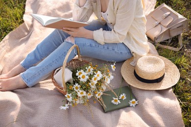 Photo of Woman with bouquet of wildflowers reading book on blanket in meadow, closeup