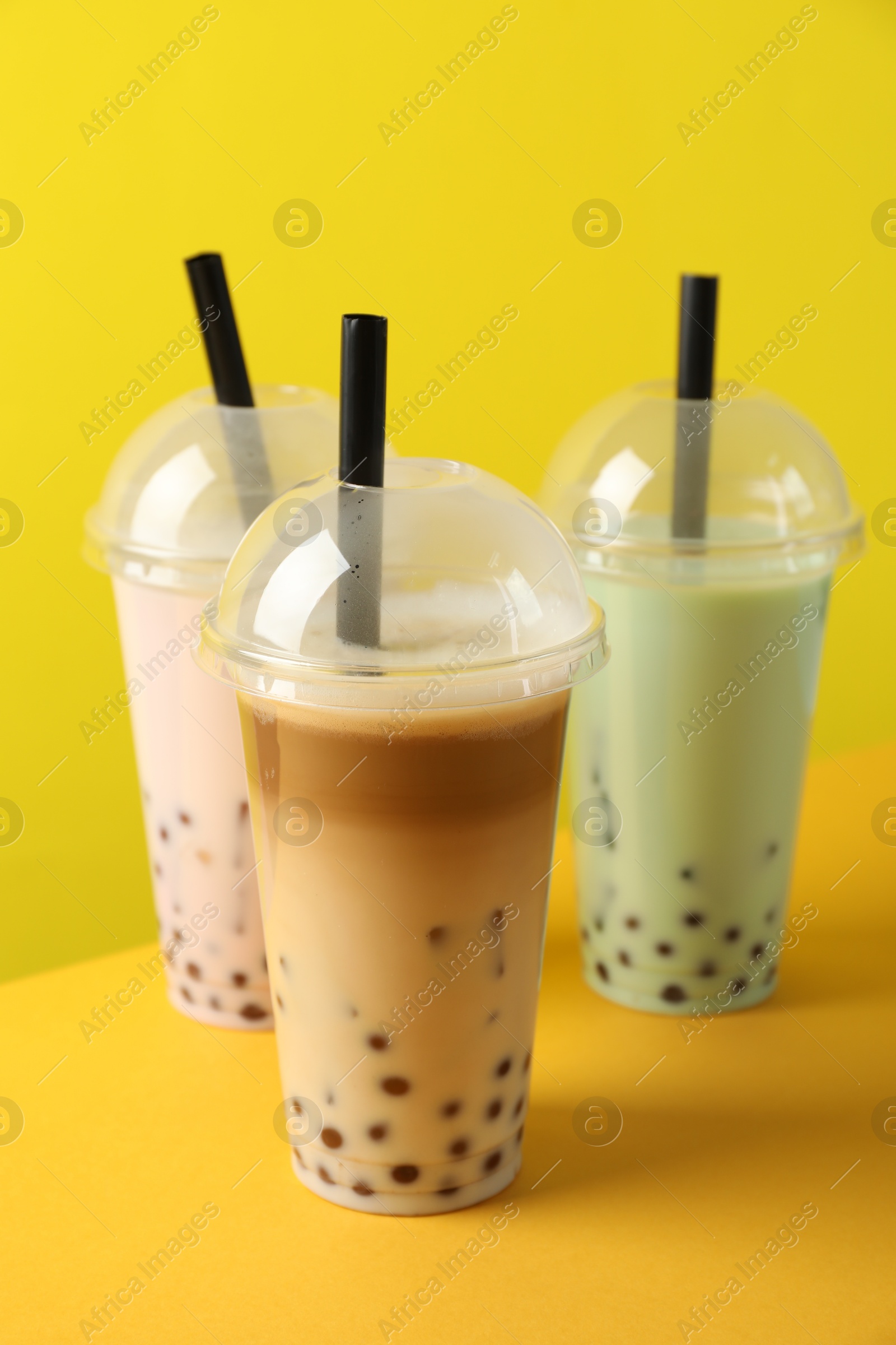 Tasty milk bubble tea in plastic cups on yellow background Photo of Tasty milk bubble tea in plastic cups on yellow background