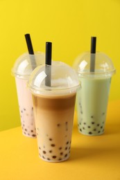 Photo of Tasty milk bubble tea in plastic cups on yellow background