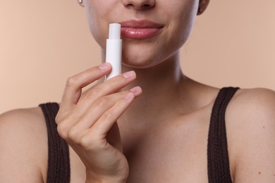 Photo of Young woman with lip balm on beige background, closeup