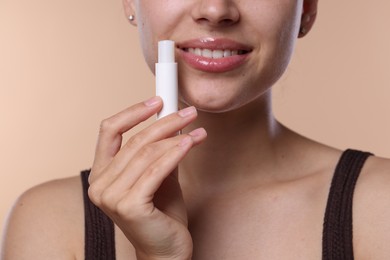 Photo of Young woman with lip balm on beige background, closeup