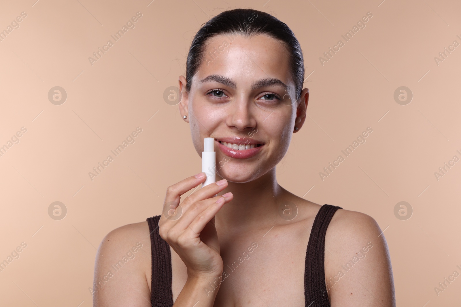 Young woman with lip balm on beige background Photo of Young woman with lip balm on beige background