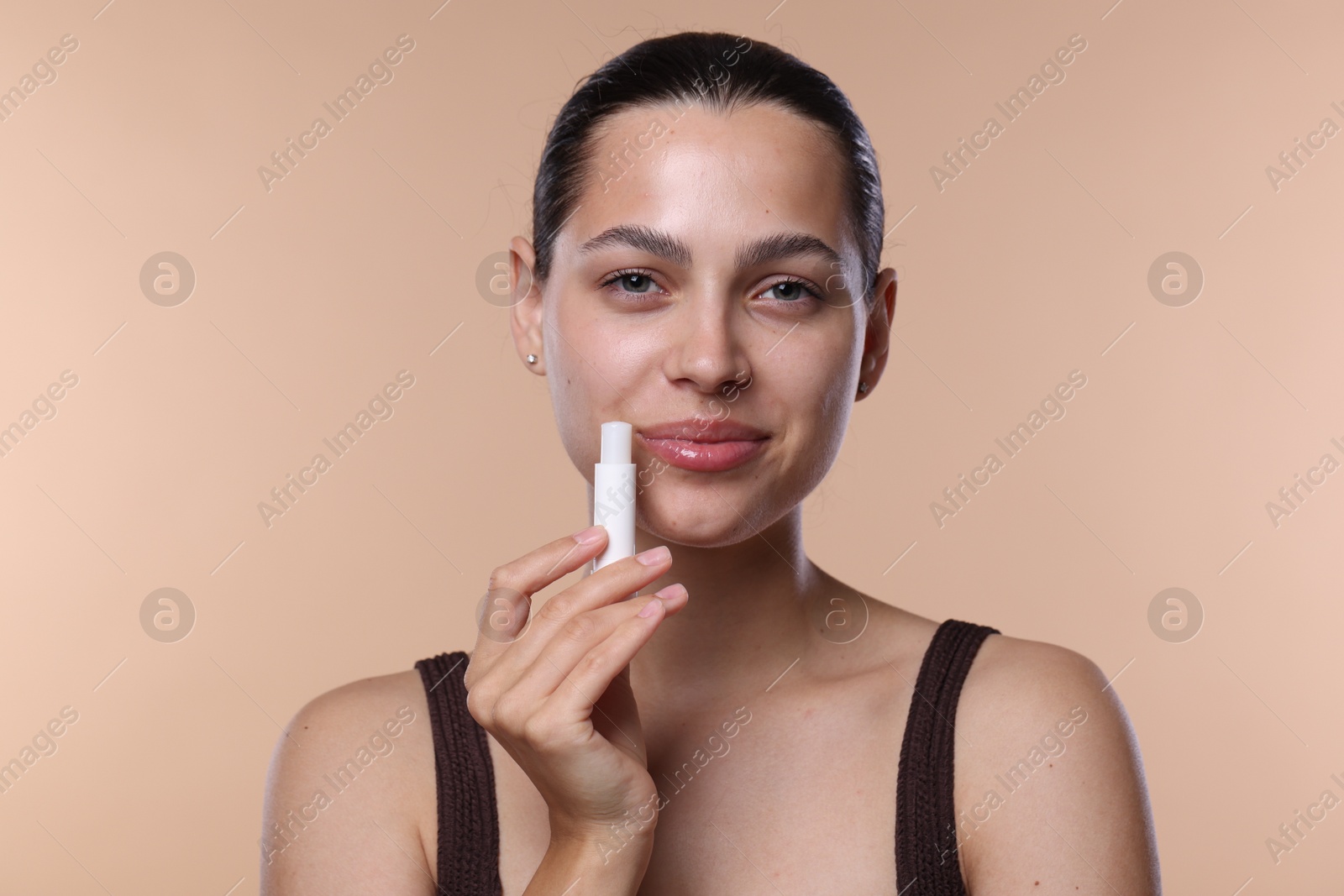 Young woman with lip balm on beige background Photo of Young woman with lip balm on beige background