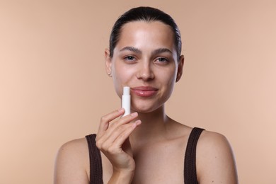 Photo of Young woman with lip balm on beige background