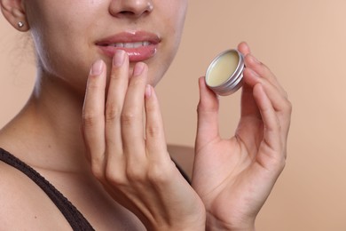 Photo of Young woman with lip balm on beige background, closeup