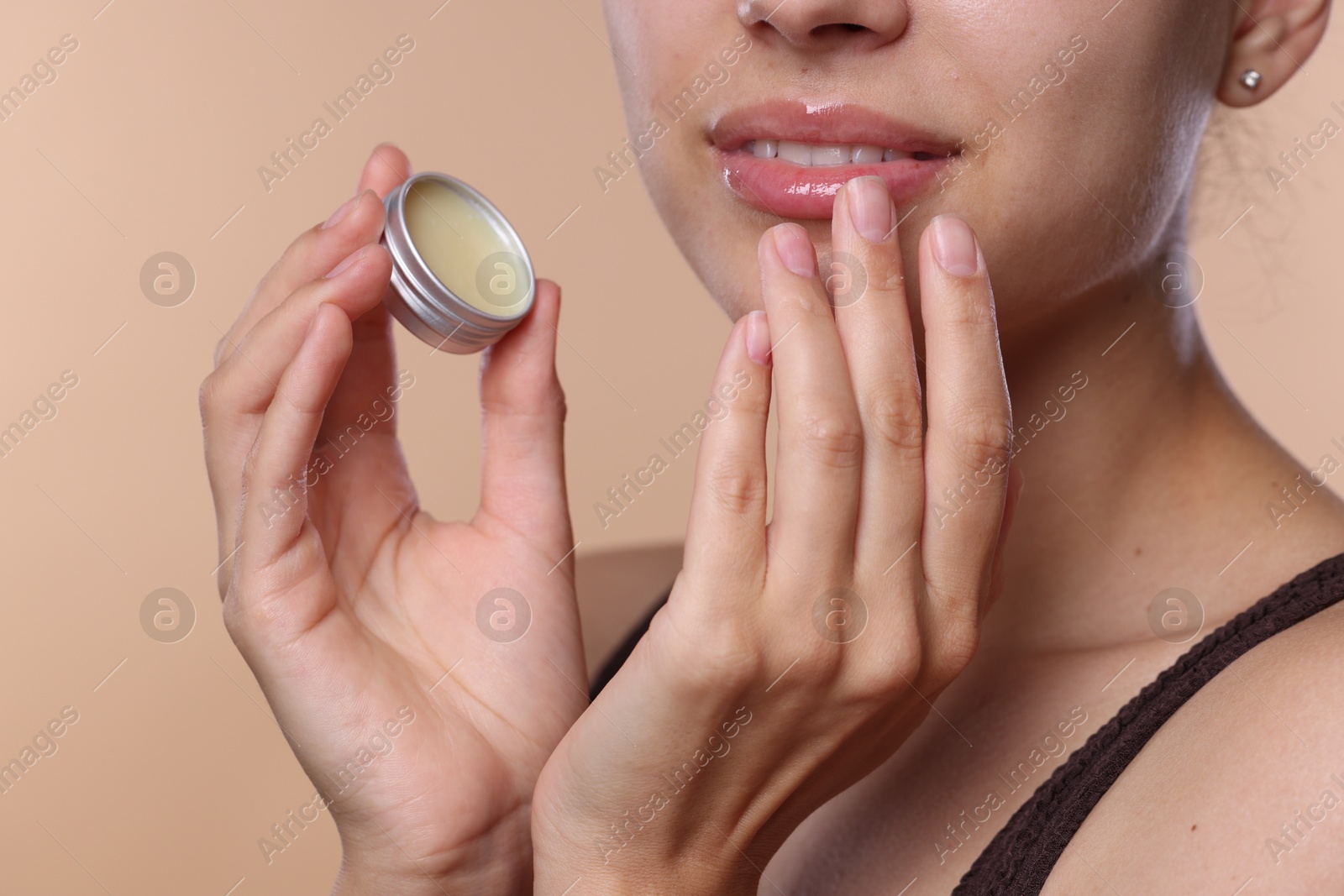 Photo of Young woman with lip balm on beige background, closeup