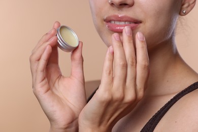 Photo of Young woman with lip balm on beige background, closeup