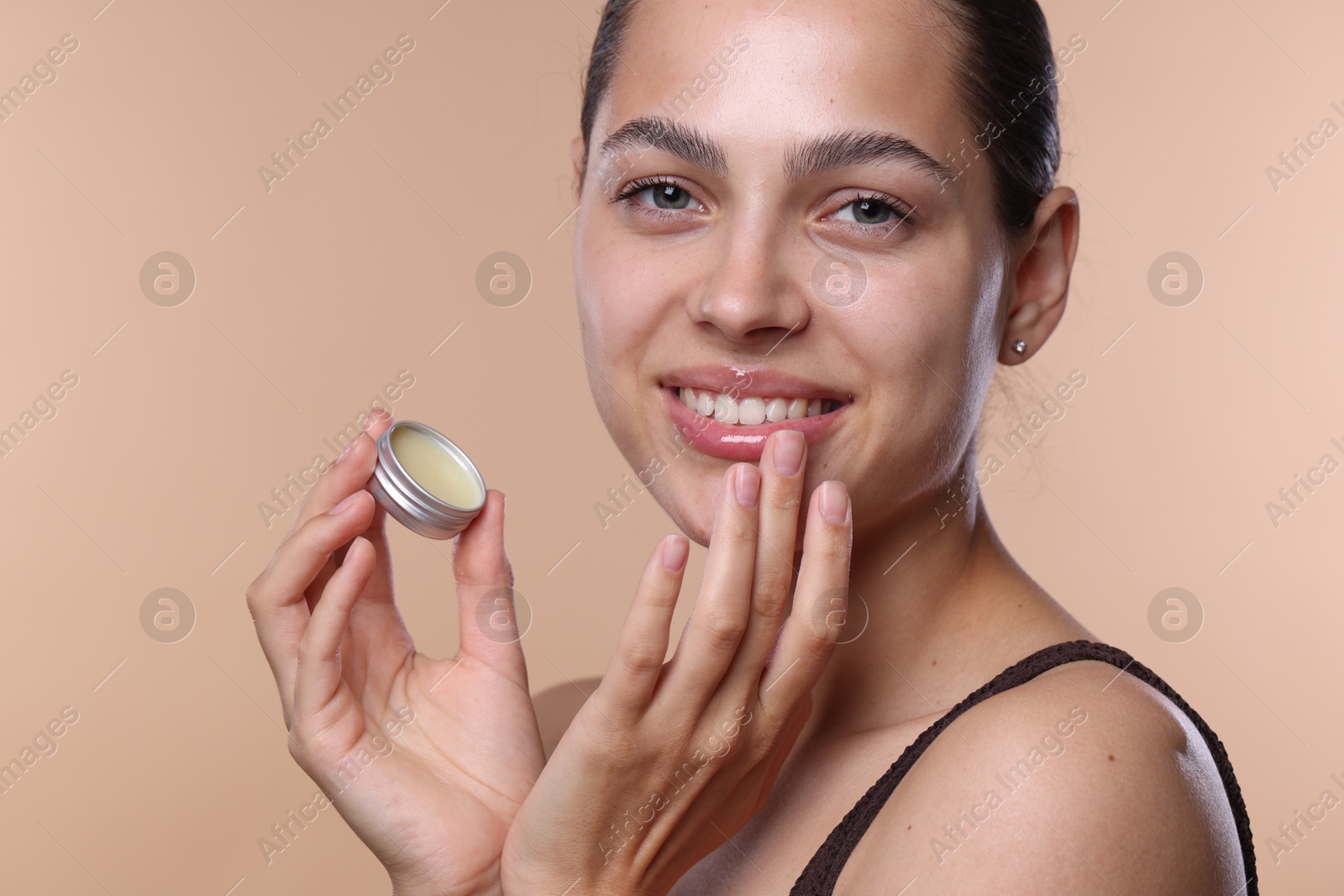 Young woman with lip balm on beige background Photo of Young woman with lip balm on beige background