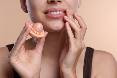 Photo of Young woman with lip balm on beige background, closeup