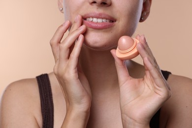Photo of Young woman with lip balm on beige background, closeup