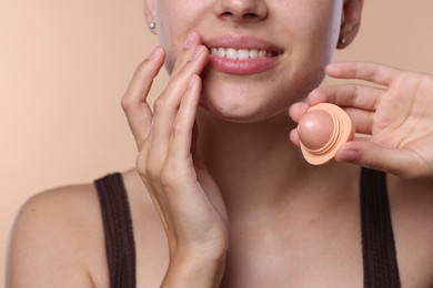 Photo of Young woman with lip balm on beige background, closeup