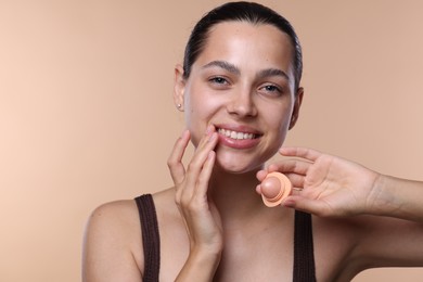 Photo of Young woman with lip balm on beige background