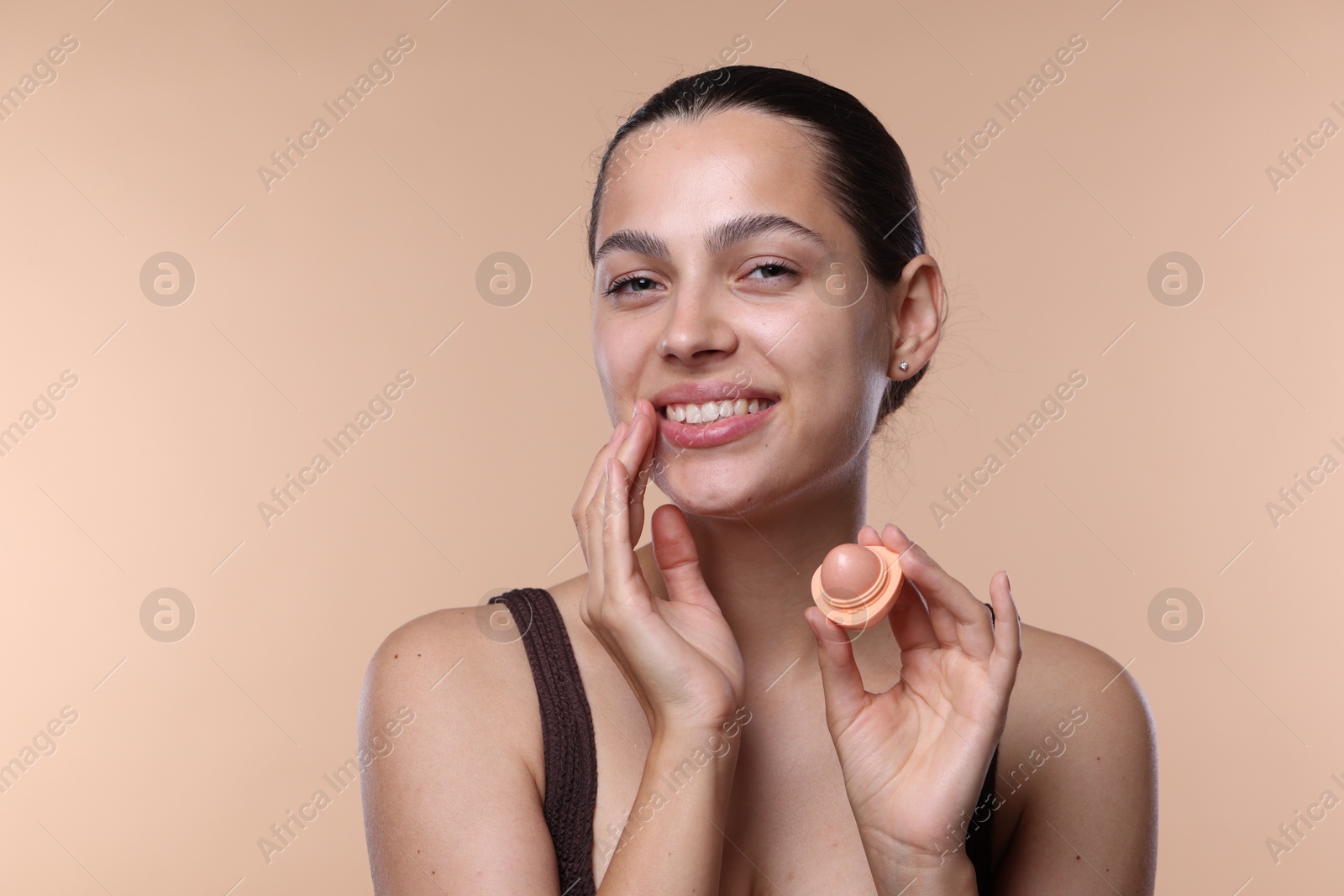 Young woman with lip balm on beige background Photo of Young woman with lip balm on beige background