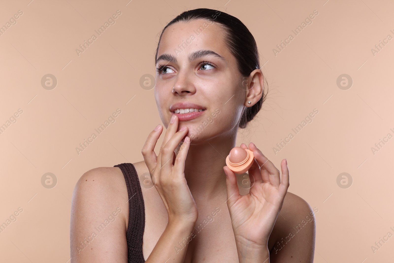 Young woman with lip balm on beige background Photo of Young woman with lip balm on beige background
