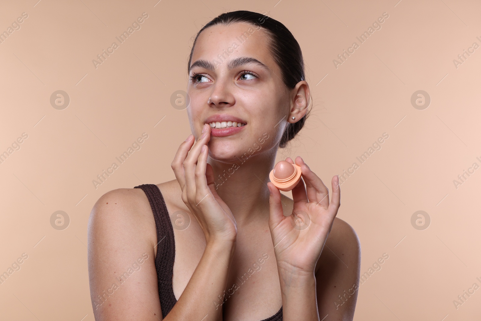 Young woman with lip balm on beige background Photo of Young woman with lip balm on beige background