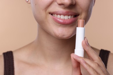 Photo of Young woman with lip balm on beige background, closeup