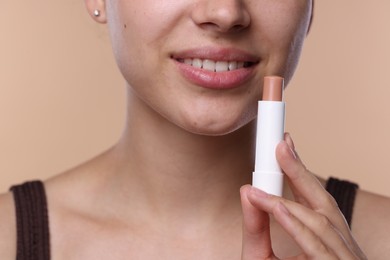 Photo of Young woman with lip balm on beige background, closeup