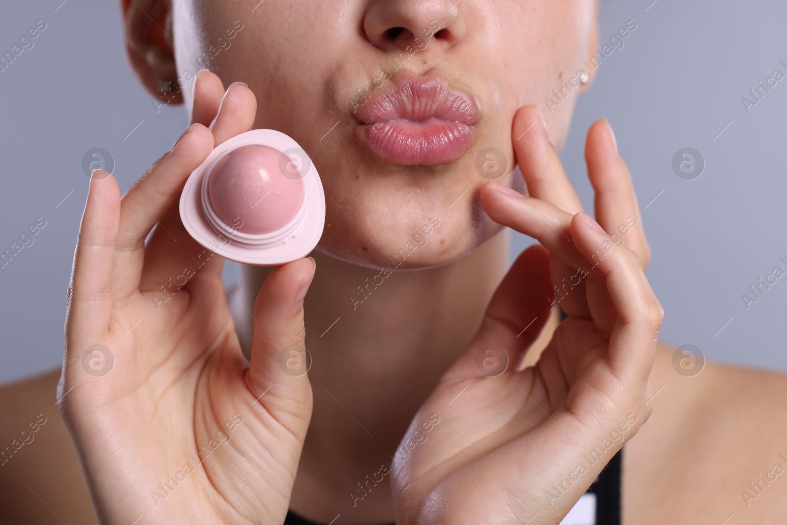 Young woman with lip balm on light grey background, closeup Photo of Young woman with lip balm on light grey background, closeup