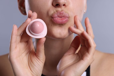 Photo of Young woman with lip balm on light grey background, closeup