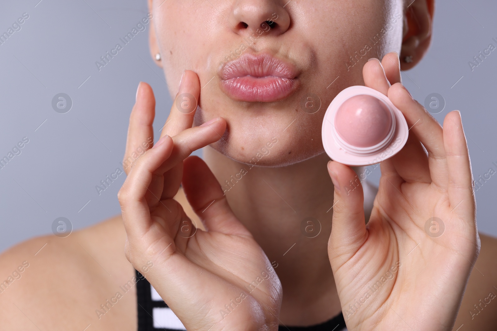 Young woman with lip balm on light grey background, closeup Photo of Young woman with lip balm on light grey background, closeup