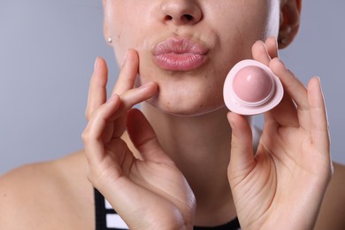 Photo of Young woman with lip balm on light grey background, closeup