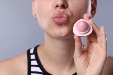 Photo of Young woman with lip balm on light grey background, closeup