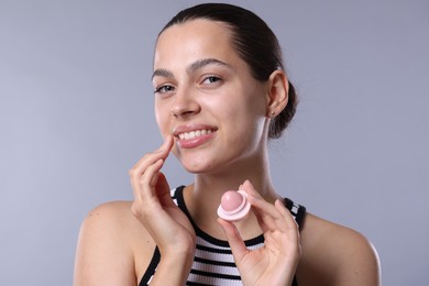 Photo of Young woman with lip balm on light grey background