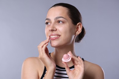 Photo of Young woman with lip balm on light grey background