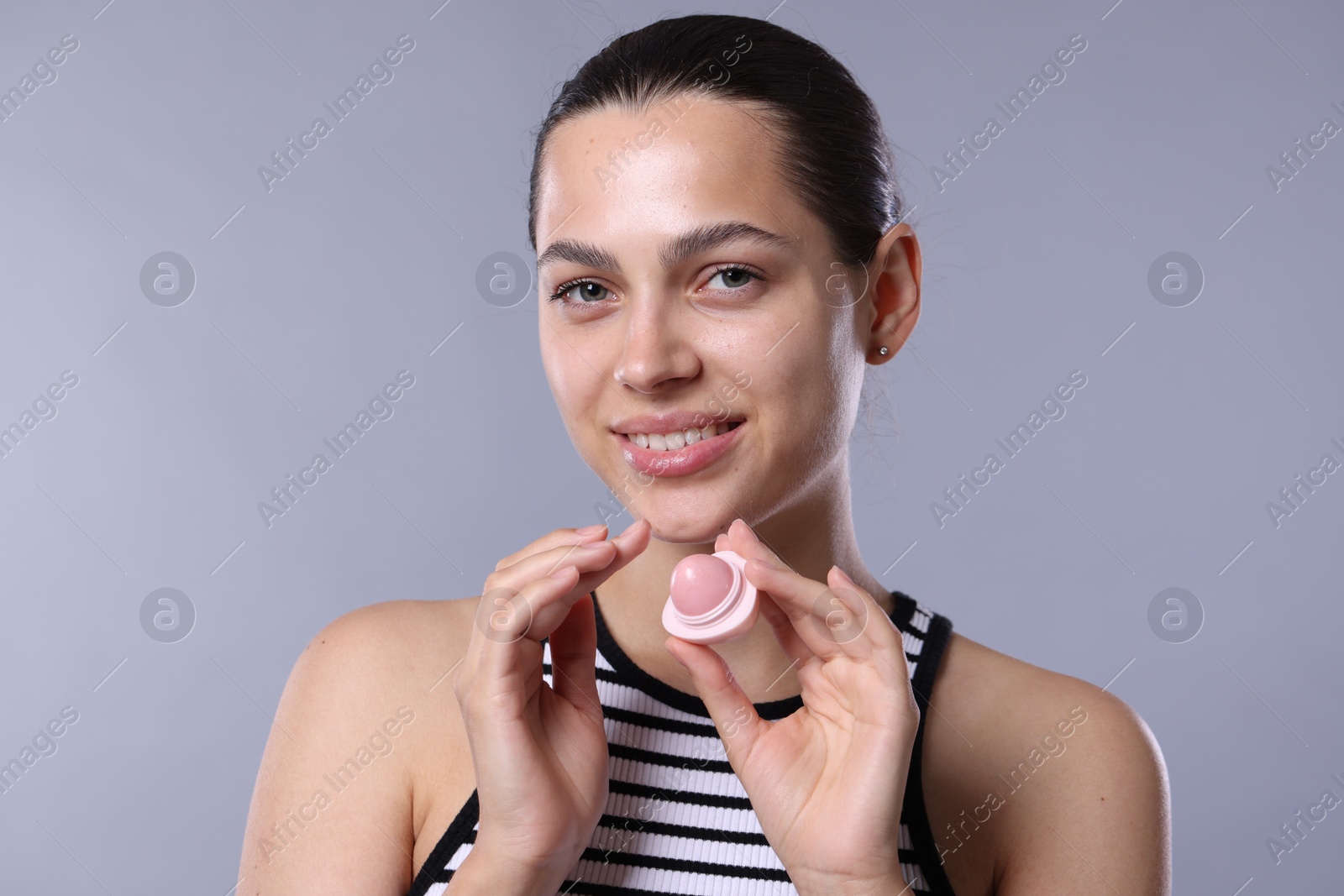 Young woman with lip balm on light grey background Photo of Young woman with lip balm on light grey background