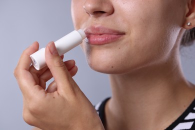 Photo of Young woman with lip balm on light grey background, closeup