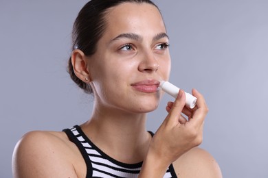 Photo of Young woman with lip balm on light grey background