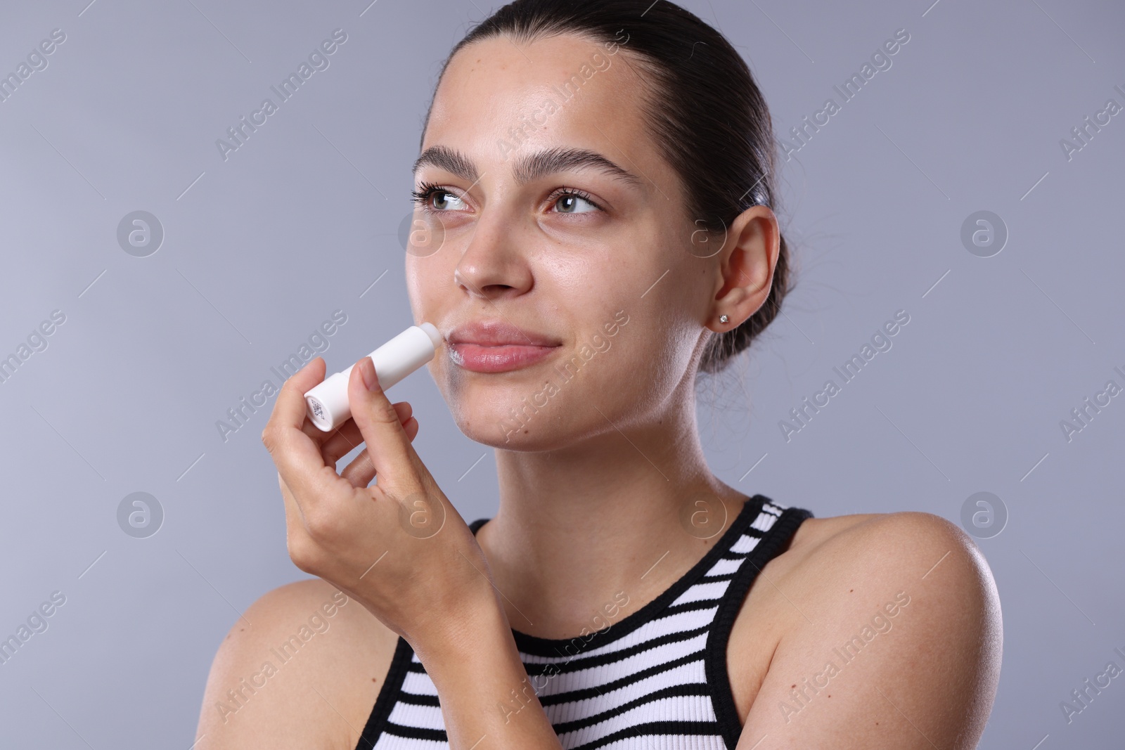 Young woman with lip balm on light grey background Photo of Young woman with lip balm on light grey background