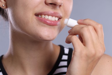 Photo of Young woman with lip balm on light grey background, closeup