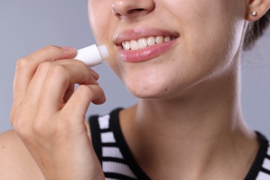 Photo of Young woman with lip balm on light grey background, closeup
