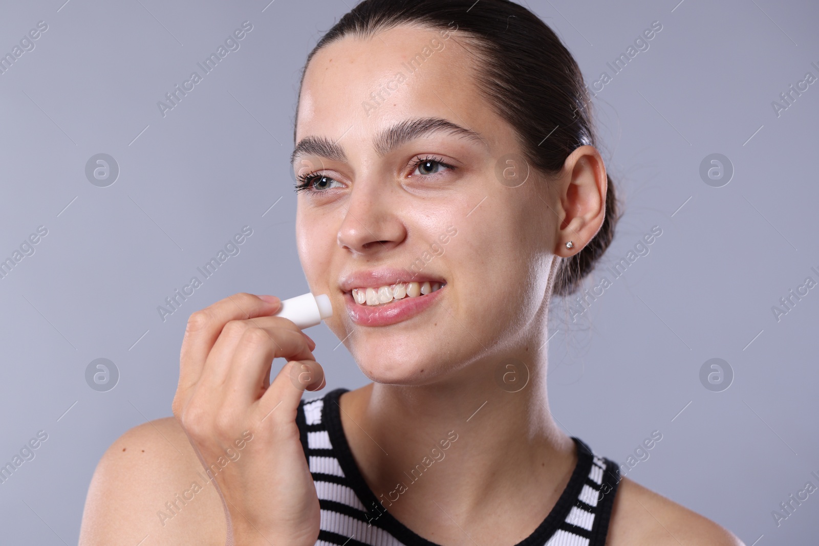 Photo of Young woman with lip balm on light grey background
