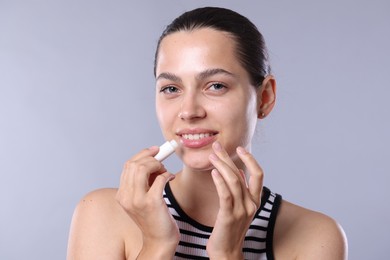 Photo of Young woman with lip balm on light grey background