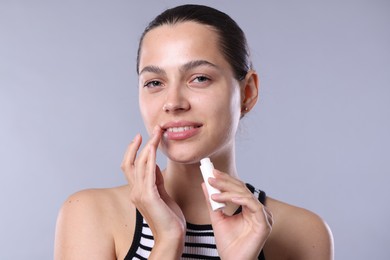 Photo of Young woman with lip balm on light grey background