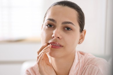Photo of Young woman with lip balm at home