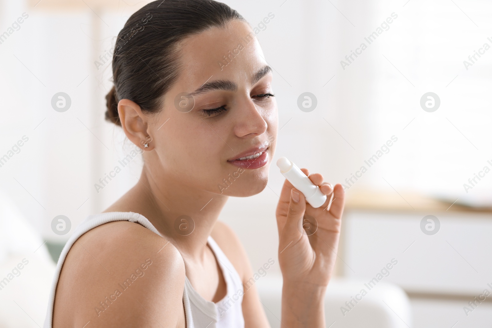Young woman with lip balm at home Photo of Young woman with lip balm at home