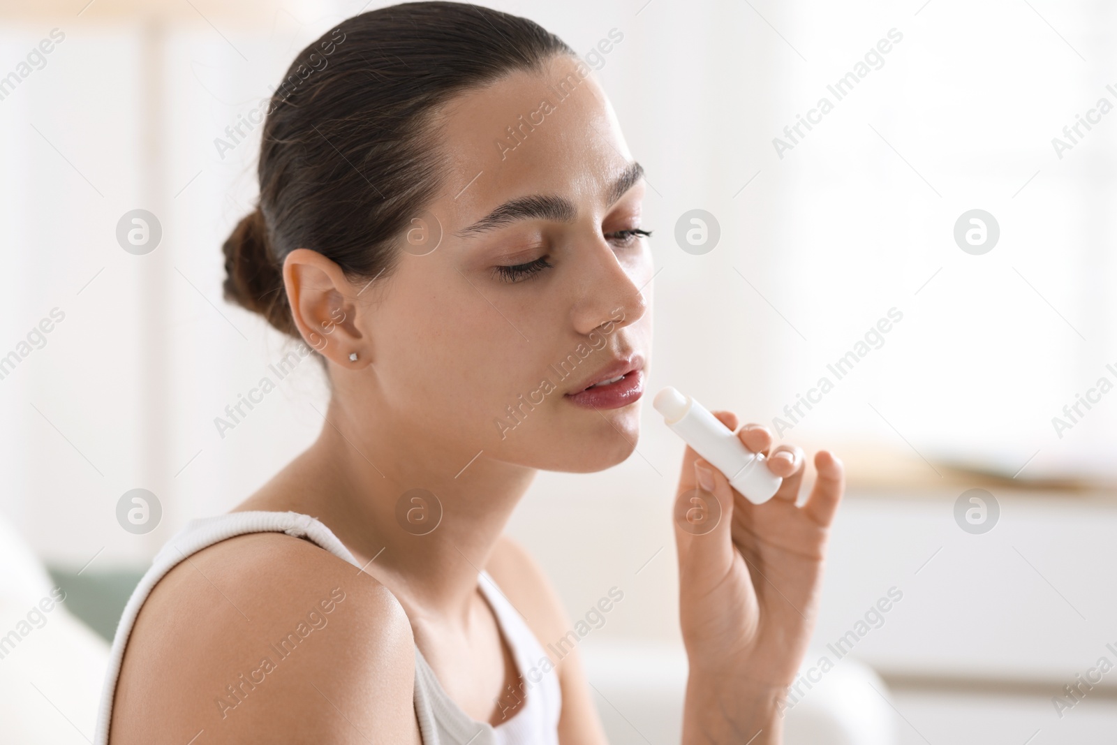 Photo of Young woman with lip balm at home