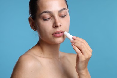 Photo of Young woman with lip balm on light blue background