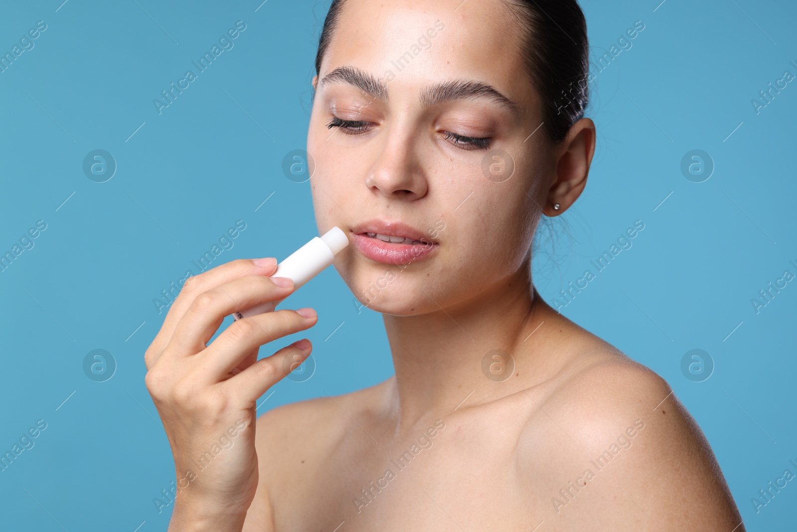 Young woman with lip balm on light blue background Photo of Young woman with lip balm on light blue background