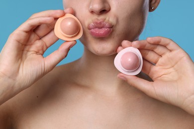 Photo of Young woman with lip balms on light blue background, closeup