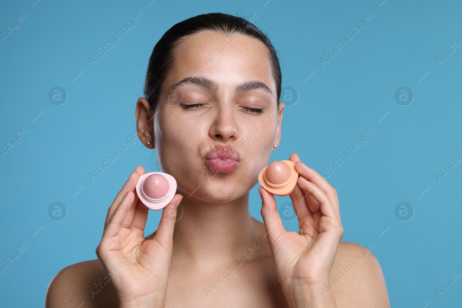 Young woman with lip balms on light blue background Photo of Young woman with lip balms on light blue background